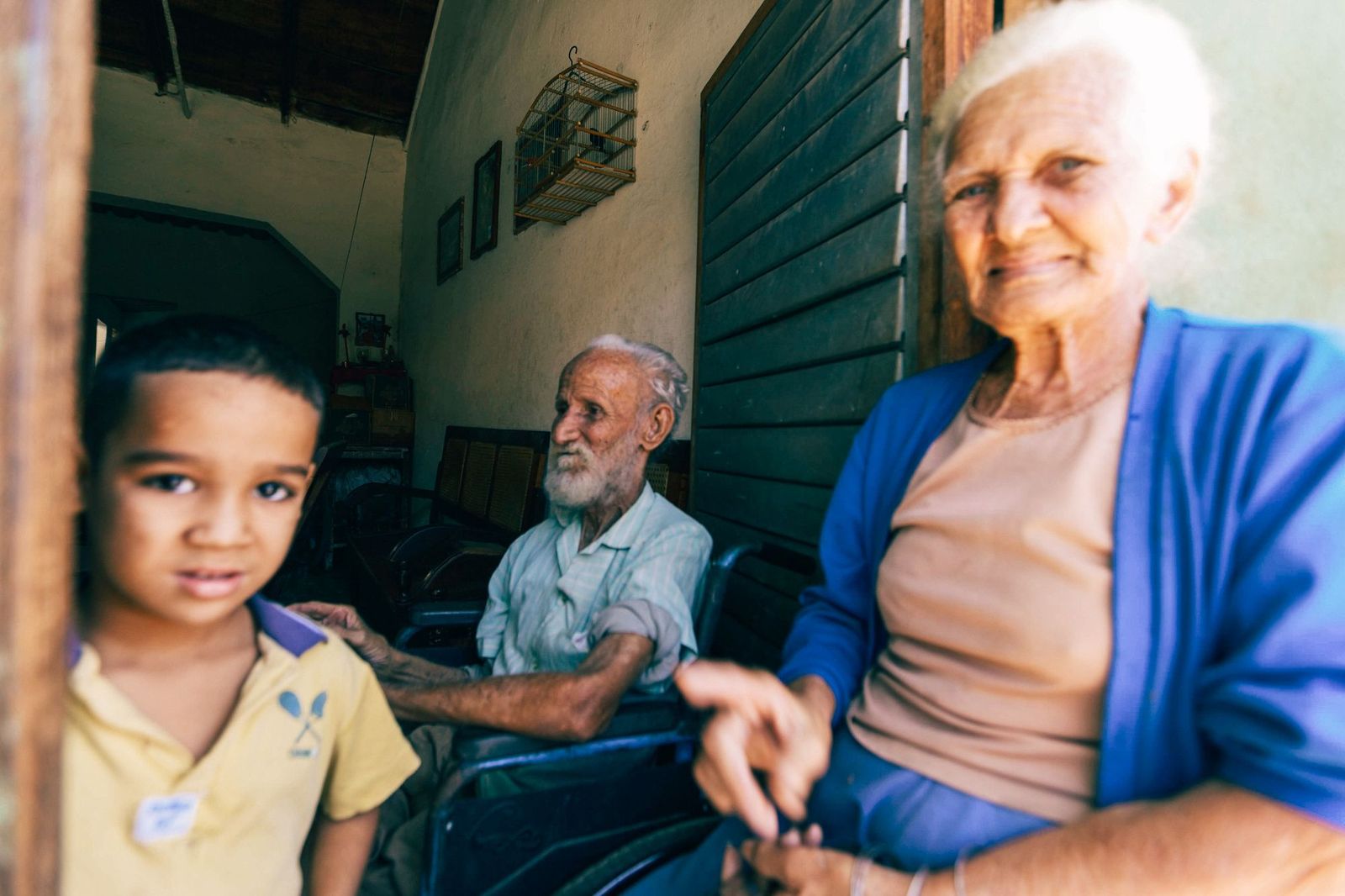 A grandmother smiles beside her husband and young grandson at home.