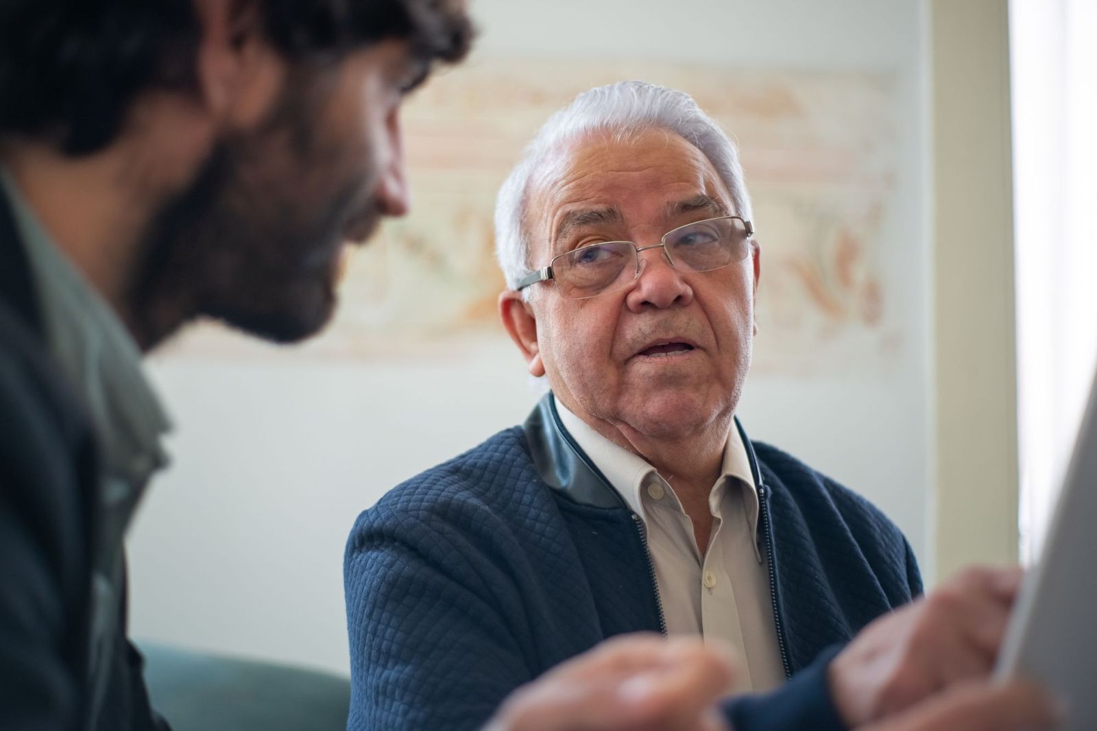 A younger man sits with an older man in glasses, having a calm and thoughtful conversation.