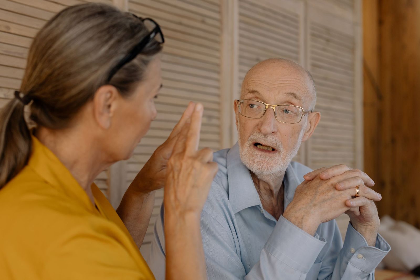 A woman talks face to face with an older man, using her hands to help explain, as he listens and responds.
